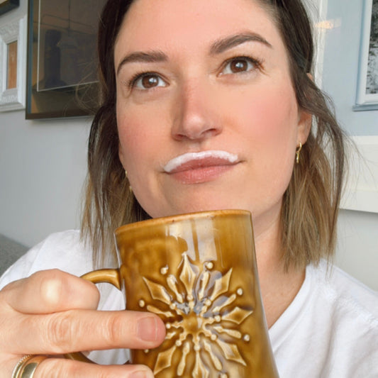Emma holding a mug of hot protein coffee with a protein foam moustache